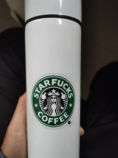 Close-up of a white travel mug featuring a humorous Starbucks parody logo with the text 'STARFUCKS COFFEE'.