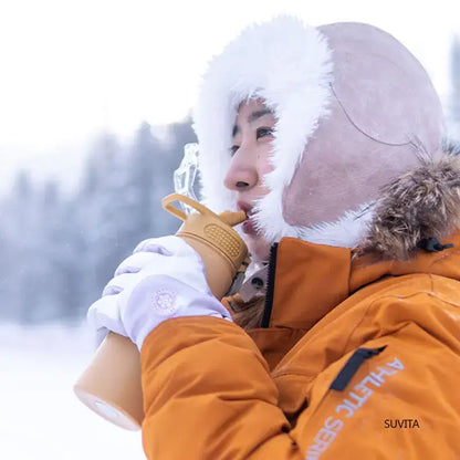 Woman drinking from a durable insulated water bottle in a snowy landscape, wearing warm winter clothing.