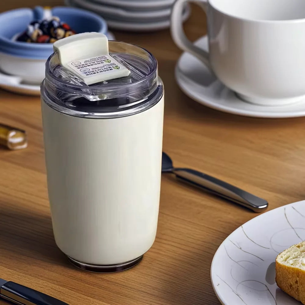 Stylish insulated travel mug on a dining table next to coffee and a plate of bread.