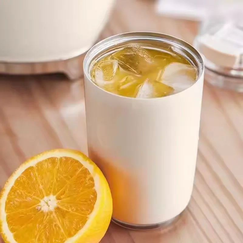 Insulated travel mug with iced beverage and fresh orange slice on wooden table.